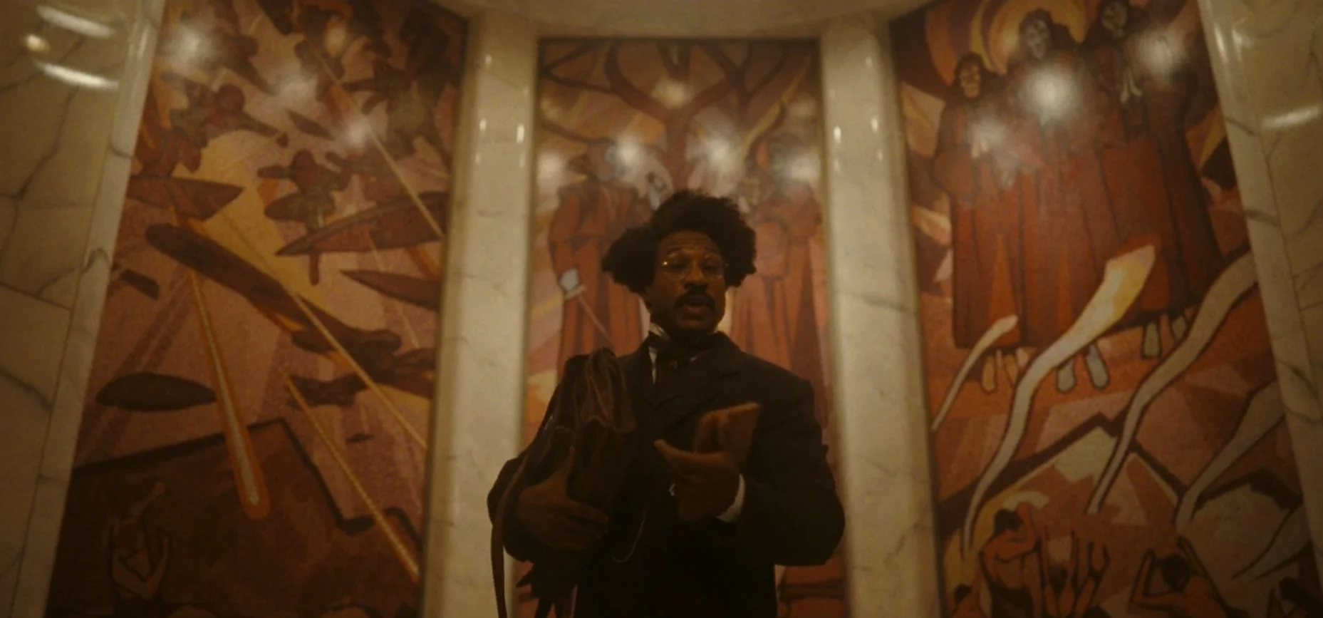 Victor Timely vor den Wandbildern zum Temporal War auf einem Szenenfoto aus der „Loki“-Episode „Das Herz der TVA“